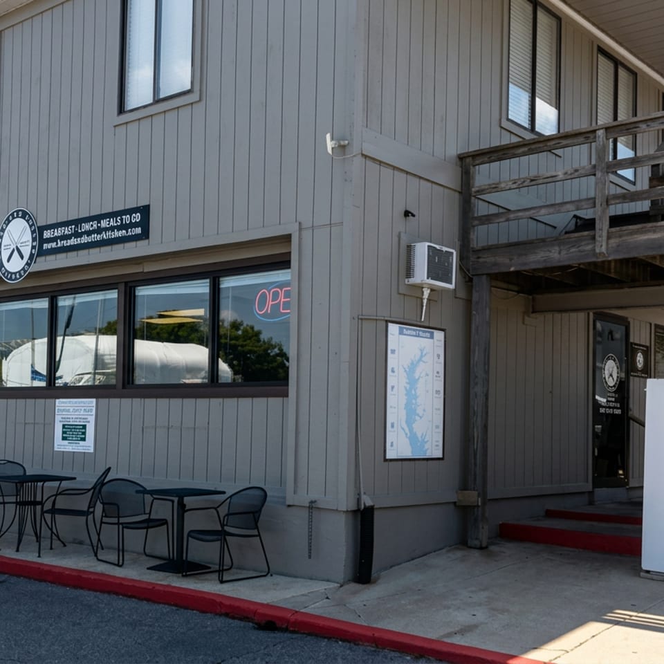 Gray restaurant exterior with outdoor tables, an open sign, entrance stairs, and an American flag.