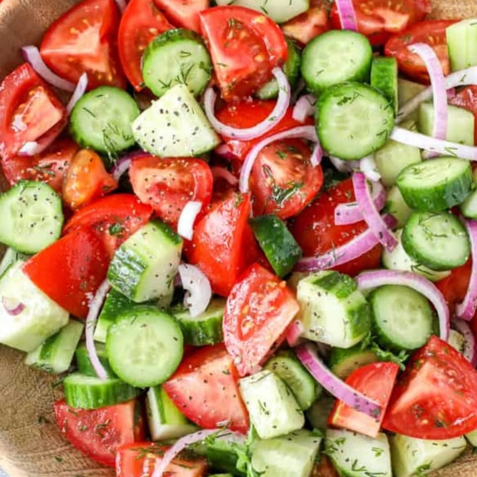 Colorful salad with chopped tomatoes, cucumbers, red onion, herbs, and seasoning in a wooden bowl.