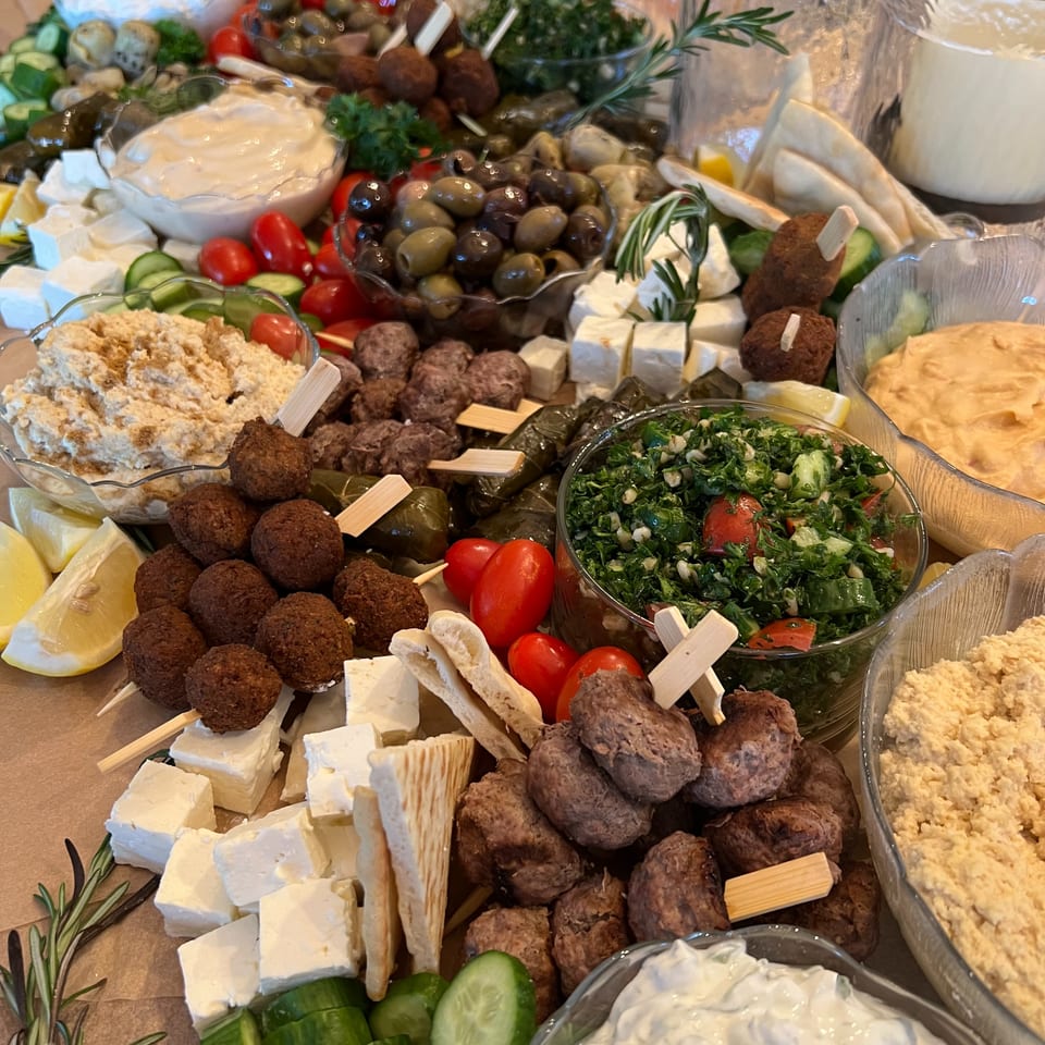 Mediterranean mezze spread with falafel, meatballs, feta, olives, hummus, tabbouleh, vegetables, pita, and creamy dips.